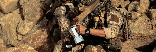 Operador táctico preparando café fuerte en una Moka con taza Duty Force Coffee durante una pausa en terreno rocoso